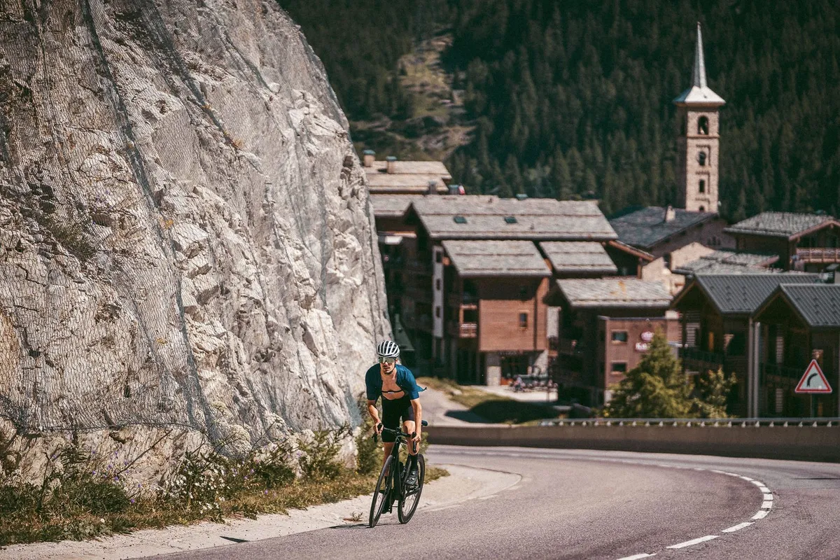 Rennradfahrer auf einer Alpenpassstraße oberhalb eines Bergdorfs